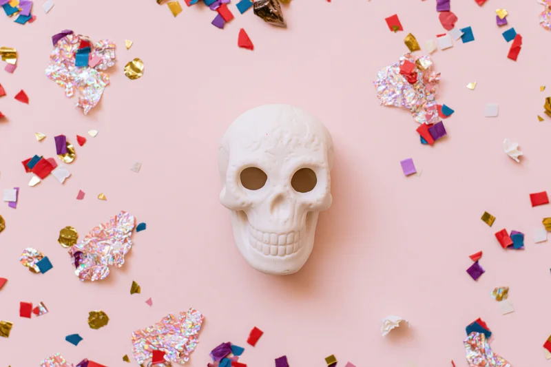 White ceramic sugar skull centered on pink surface with scattered confetti