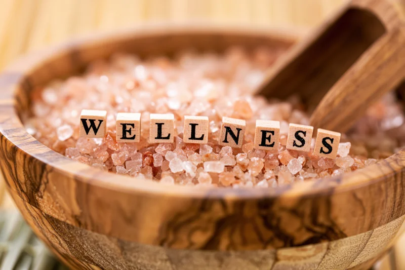 Wooden cubes spelling wellness arranged in a bowl of pink salt crystals