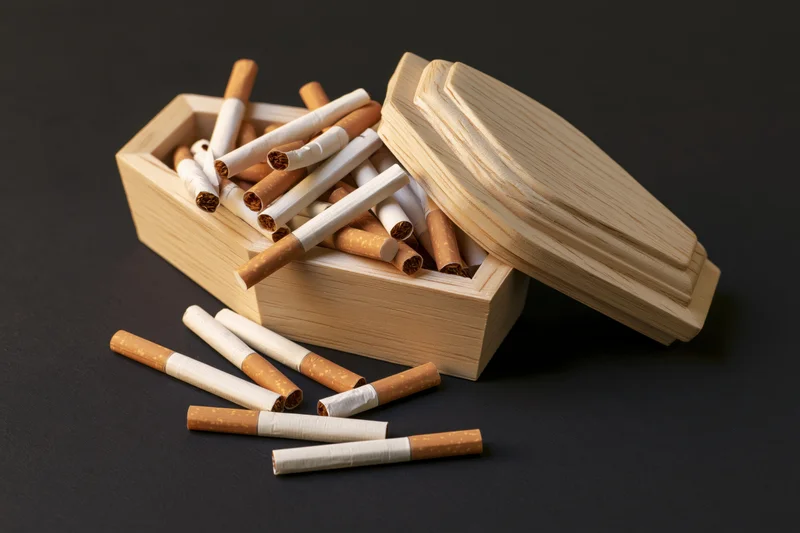 Miniature wooden coffin filled with cigarettes, lid ajar, on dark surface