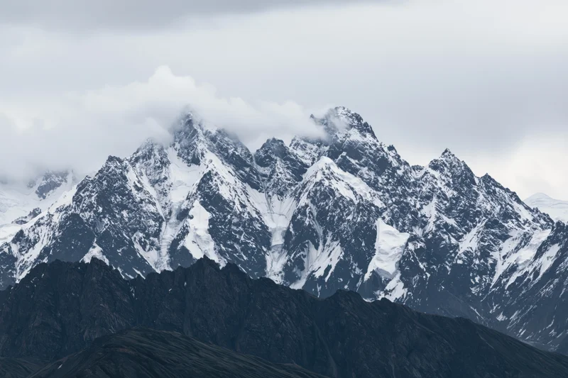 Snow-covered mountain peaks rising sharply under cloudy sky