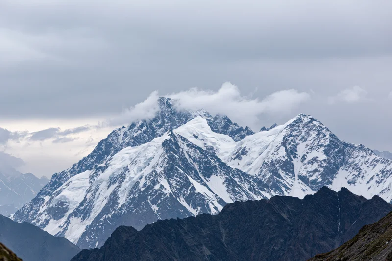 Snow-covered mountain peaks rising sharply under cloudy sky