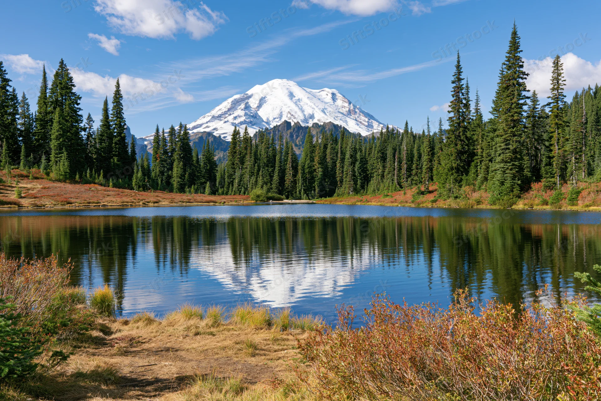 Snow-capped mountain reflected in calm lake surrounded by evergreen forest