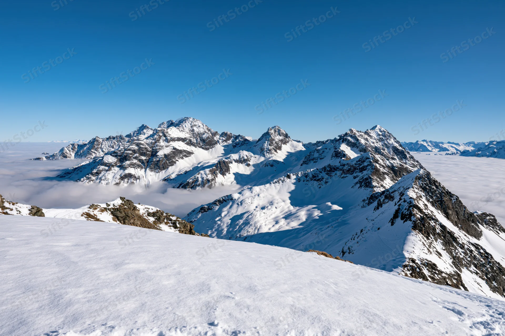 Snow-covered alpine peaks rising above a sea of low clouds under a clear blue sky