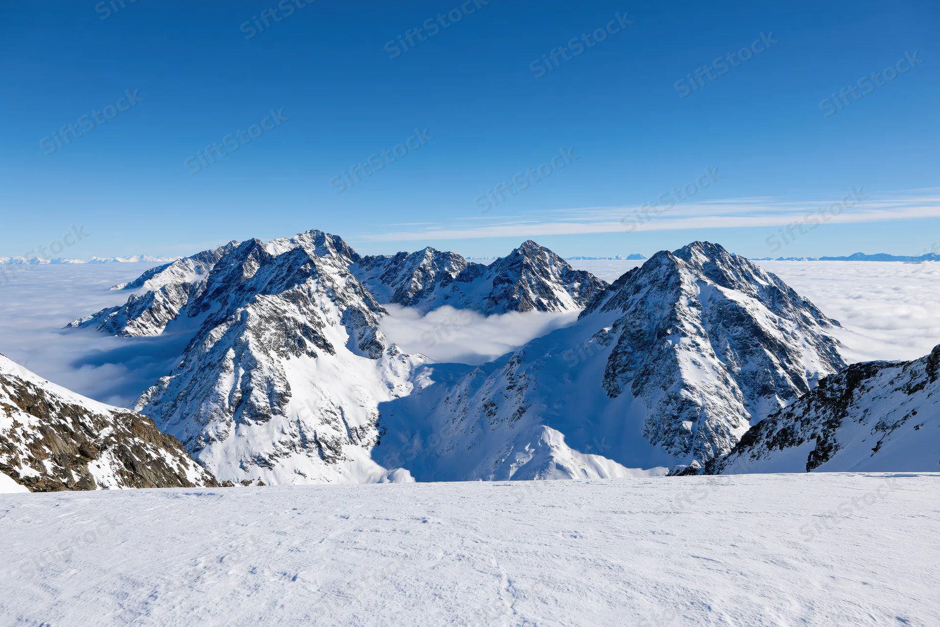 Snow-covered alpine peaks rising above a sea of low clouds under a clear blue sky