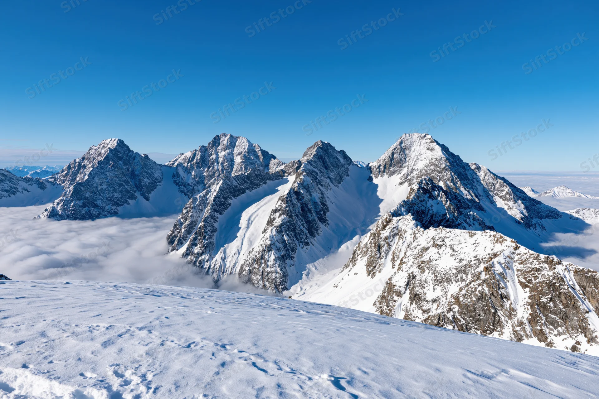 Snow-covered alpine peaks rising above a sea of clouds under a clear blue sky