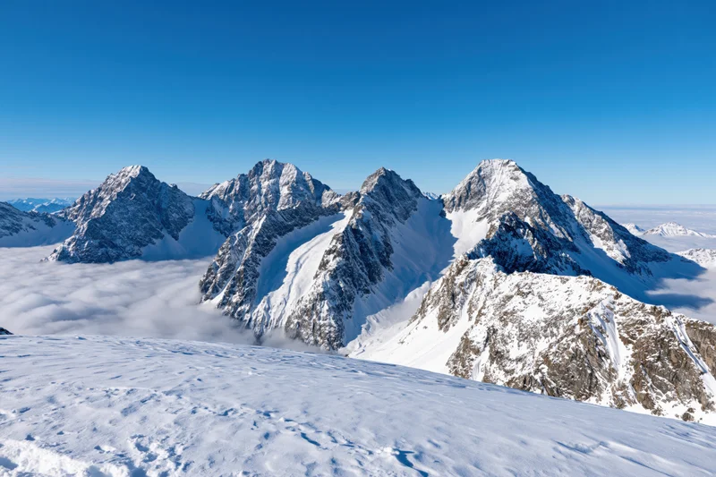Snow-covered alpine peaks rising above a sea of clouds under a clear blue sky