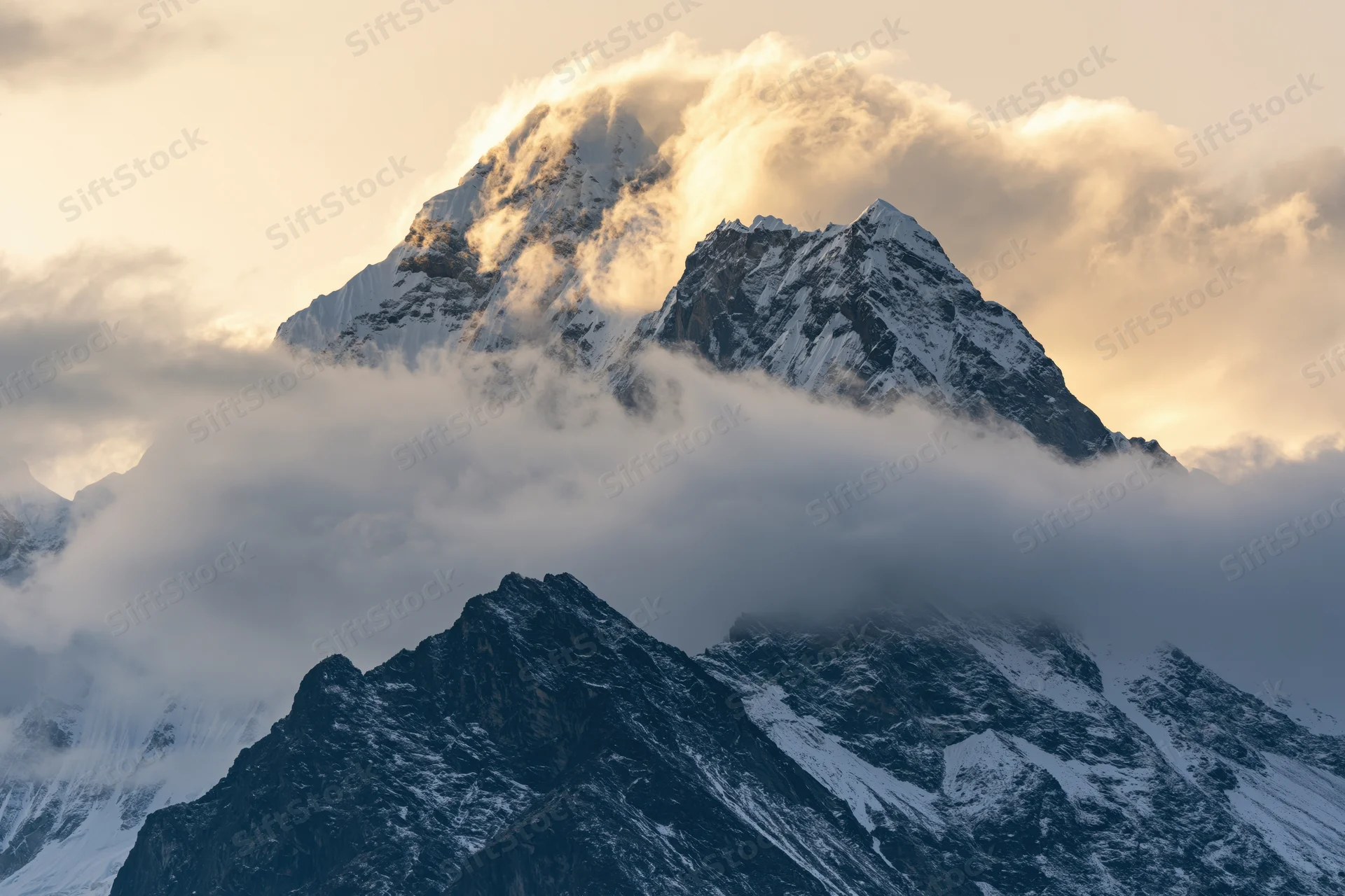 Snow-covered Himalayan peak rising above swirling clouds at sunrise