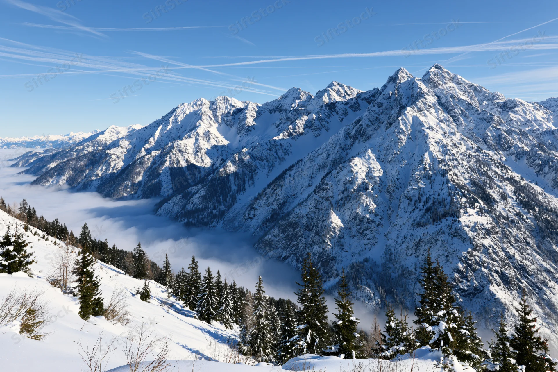 Snow-covered alpine mountains rising above a low cloud layer under a clear blue sky