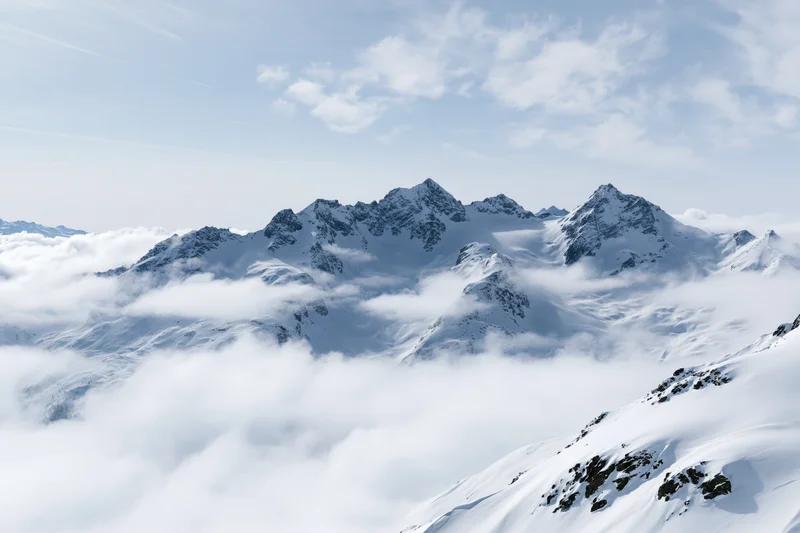 Snow-covered alpine mountain range rising above a low cloud layer under a clear sky