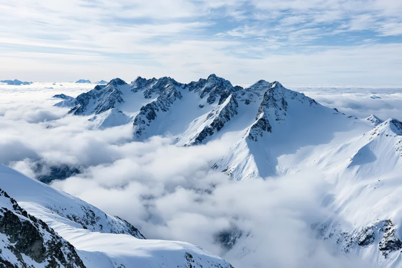 Snow-covered alpine mountain range rising above a low cloud layer