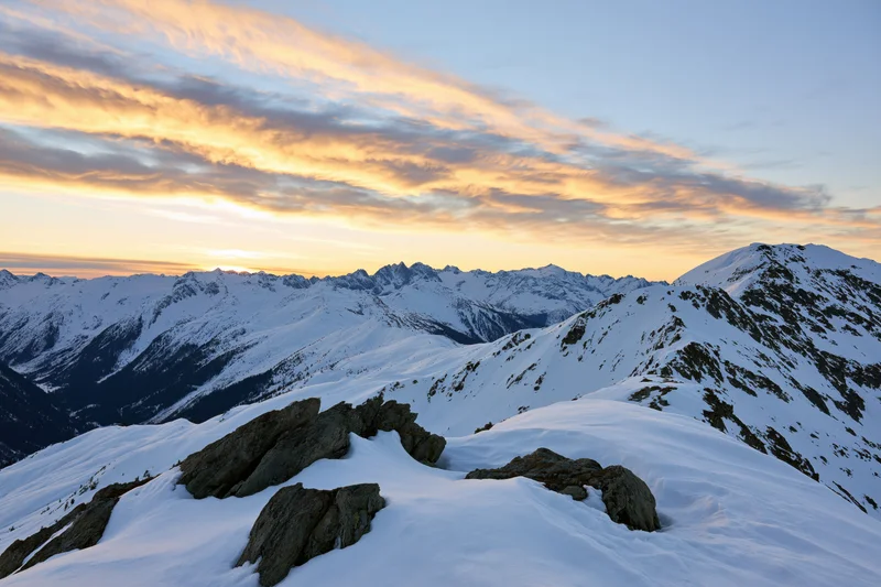 Snow-covered alpine mountain range viewed from a high ridge at sunset