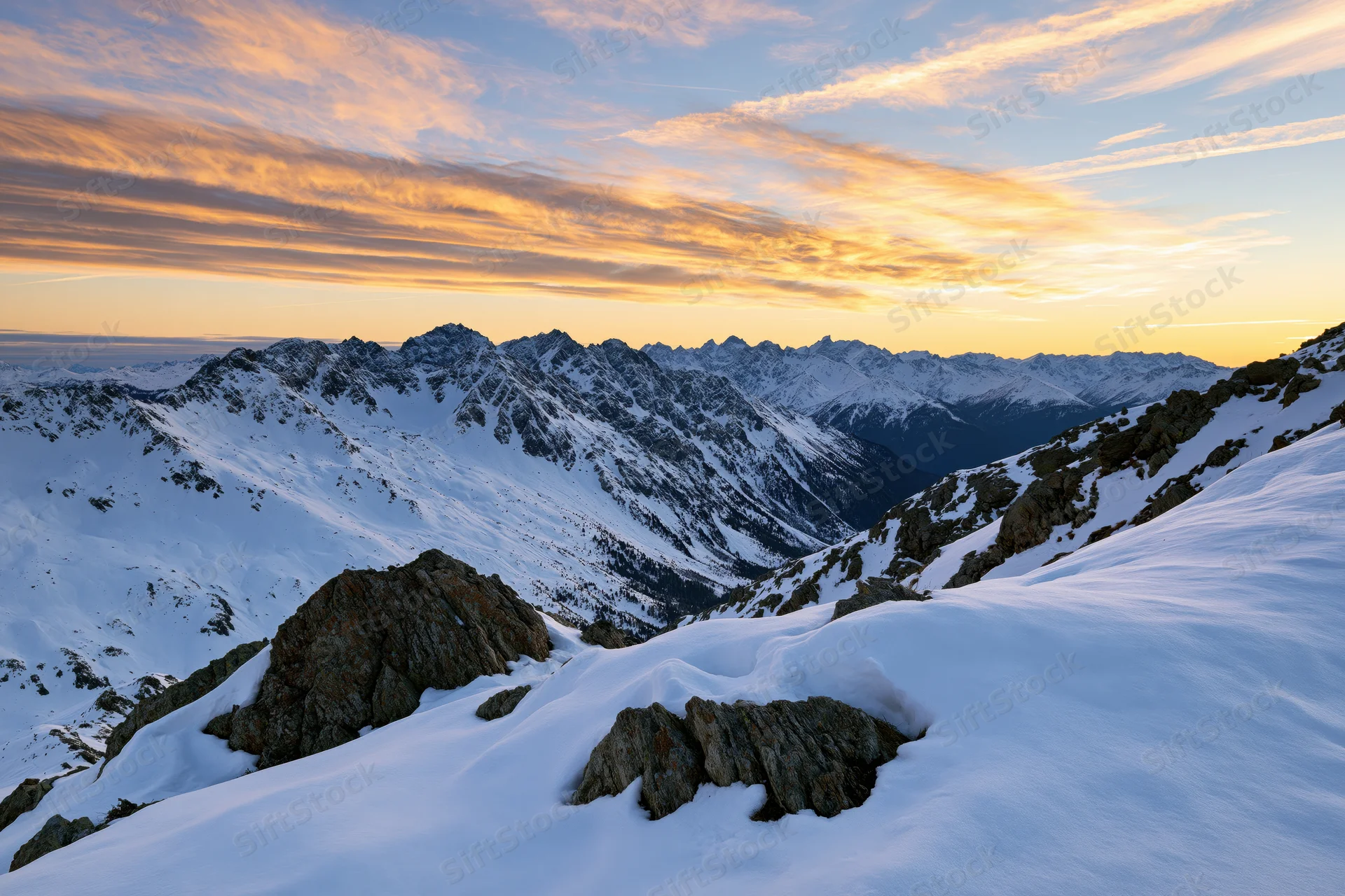 Snow-covered alpine mountain range viewed from a high ridge at sunset