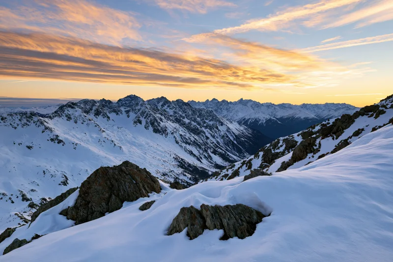 Snow-covered alpine mountain range viewed from a high ridge at sunset