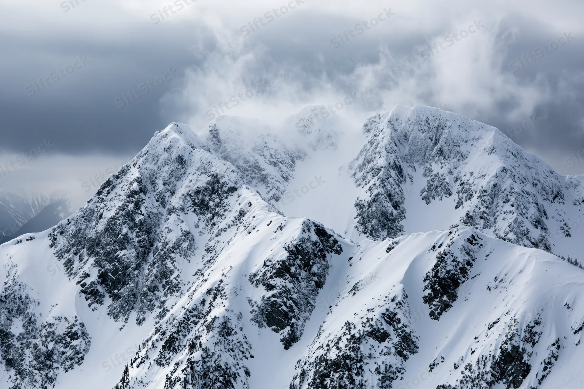 Snow-covered alpine mountain peaks with rocky ridgelines under stormy clouds