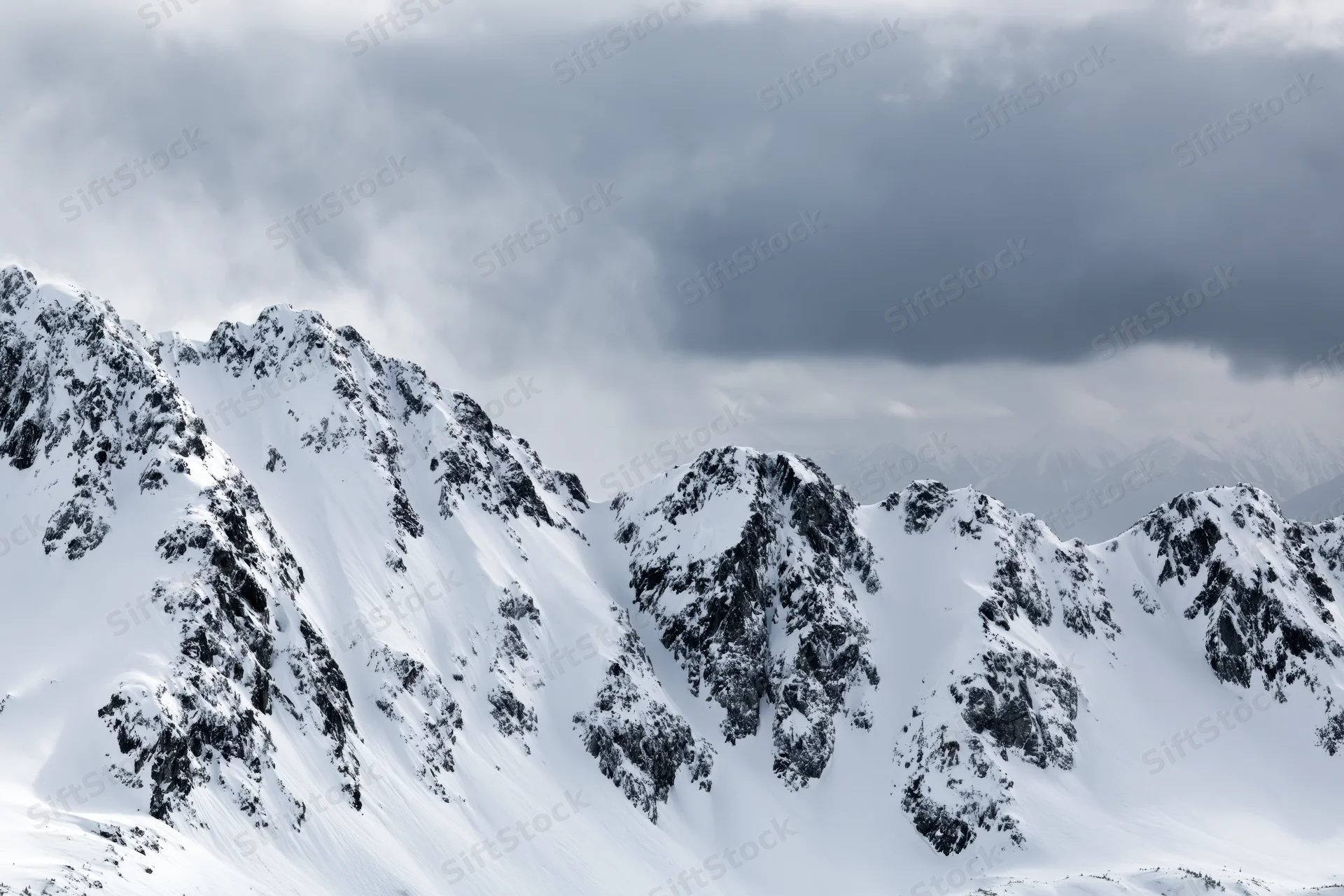 Snow-covered alpine mountain range with rocky ridgelines under overcast sky