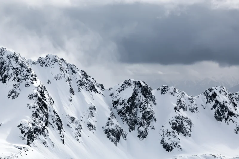 Snow-covered alpine mountain range with rocky ridgelines under overcast sky
