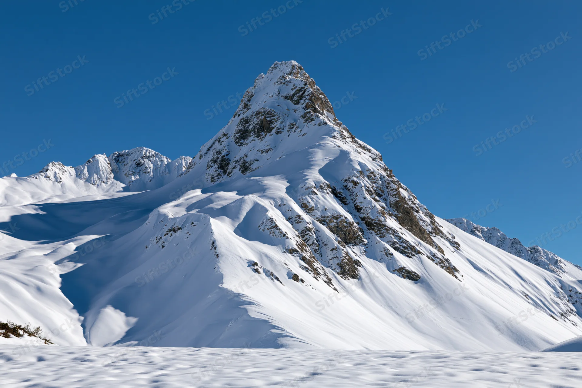 Snow-covered alpine peak rising sharply against a clear deep blue sky