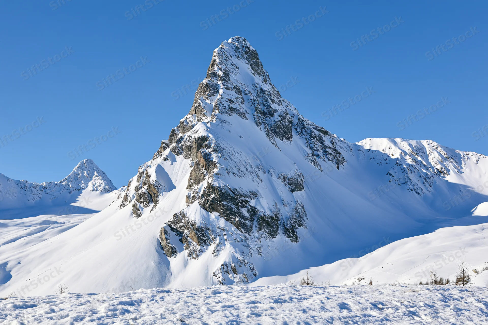 Snow-covered alpine peak rising sharply against a clear blue sky in a mountainous winter landscape
