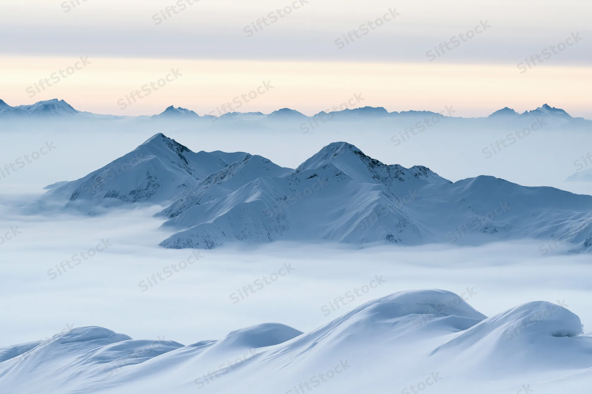 Snow-covered alpine peaks rising above a low cloud layer at dawn