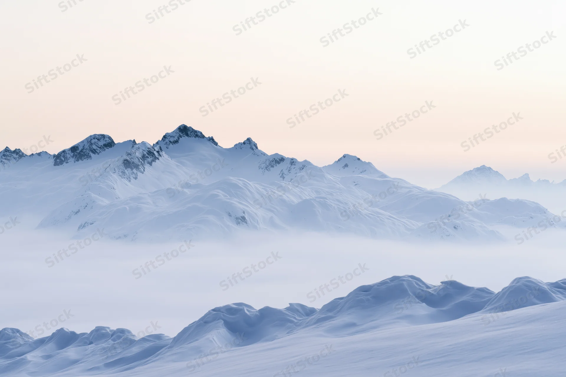 Snow-covered alpine peaks rising above a low cloud layer at dawn