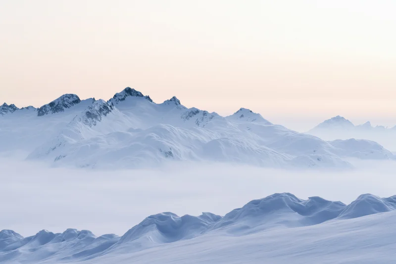 Snow-covered alpine peaks rising above a low cloud layer at dawn