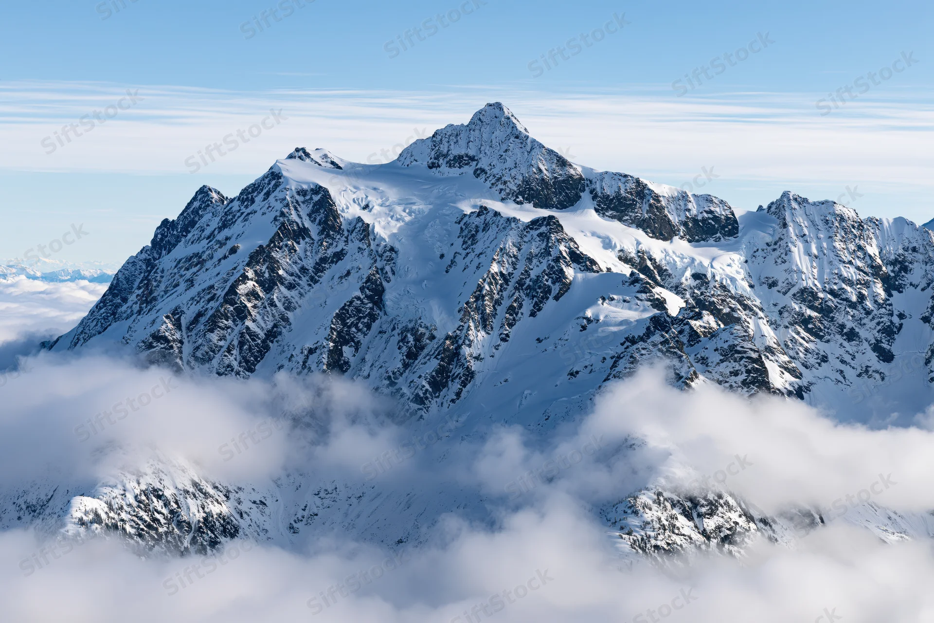 Snow-covered alpine peaks rising above a sea of low clouds under a clear blue sky