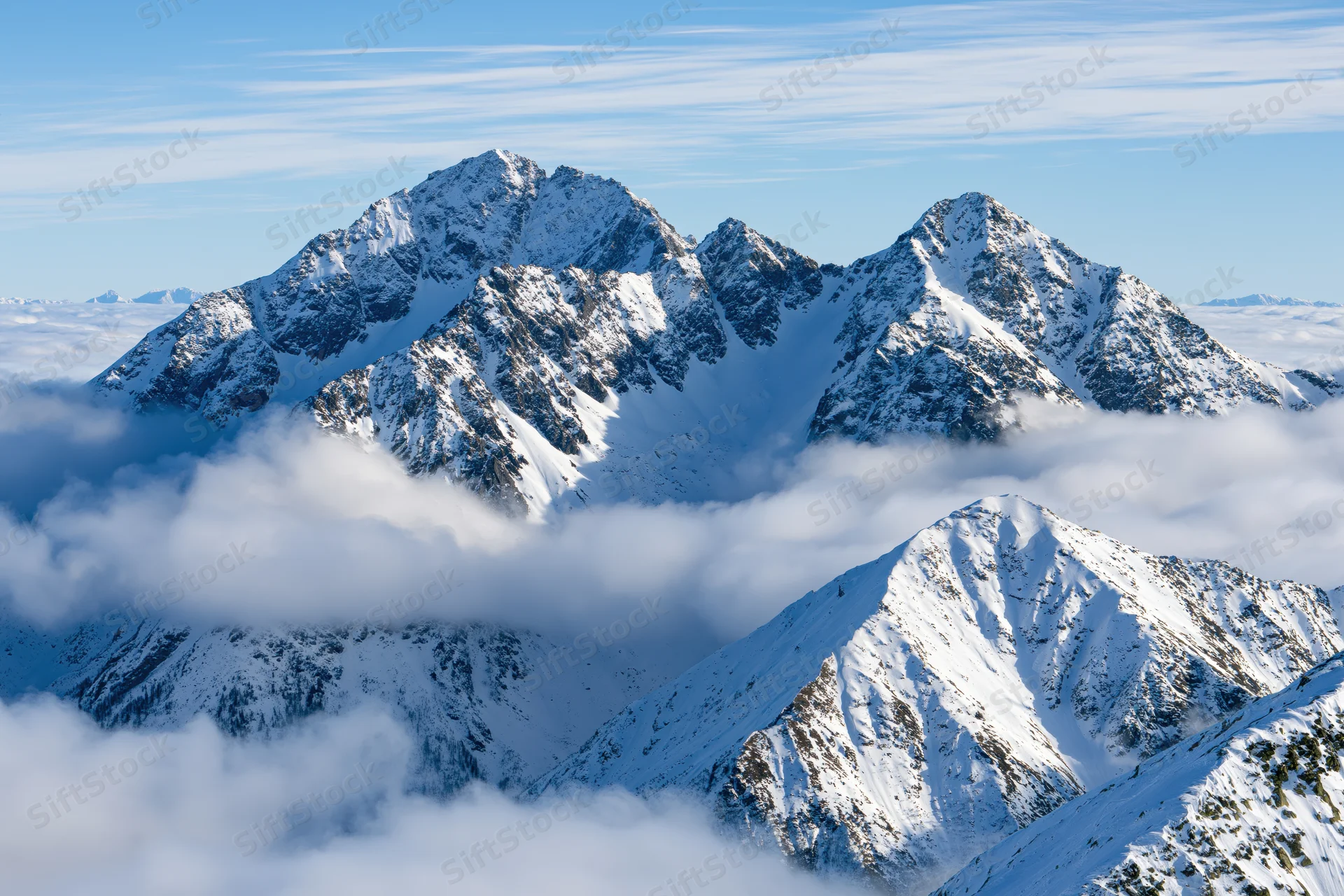 Snow-covered alpine peaks rising above a sea of low clouds under a clear blue sky