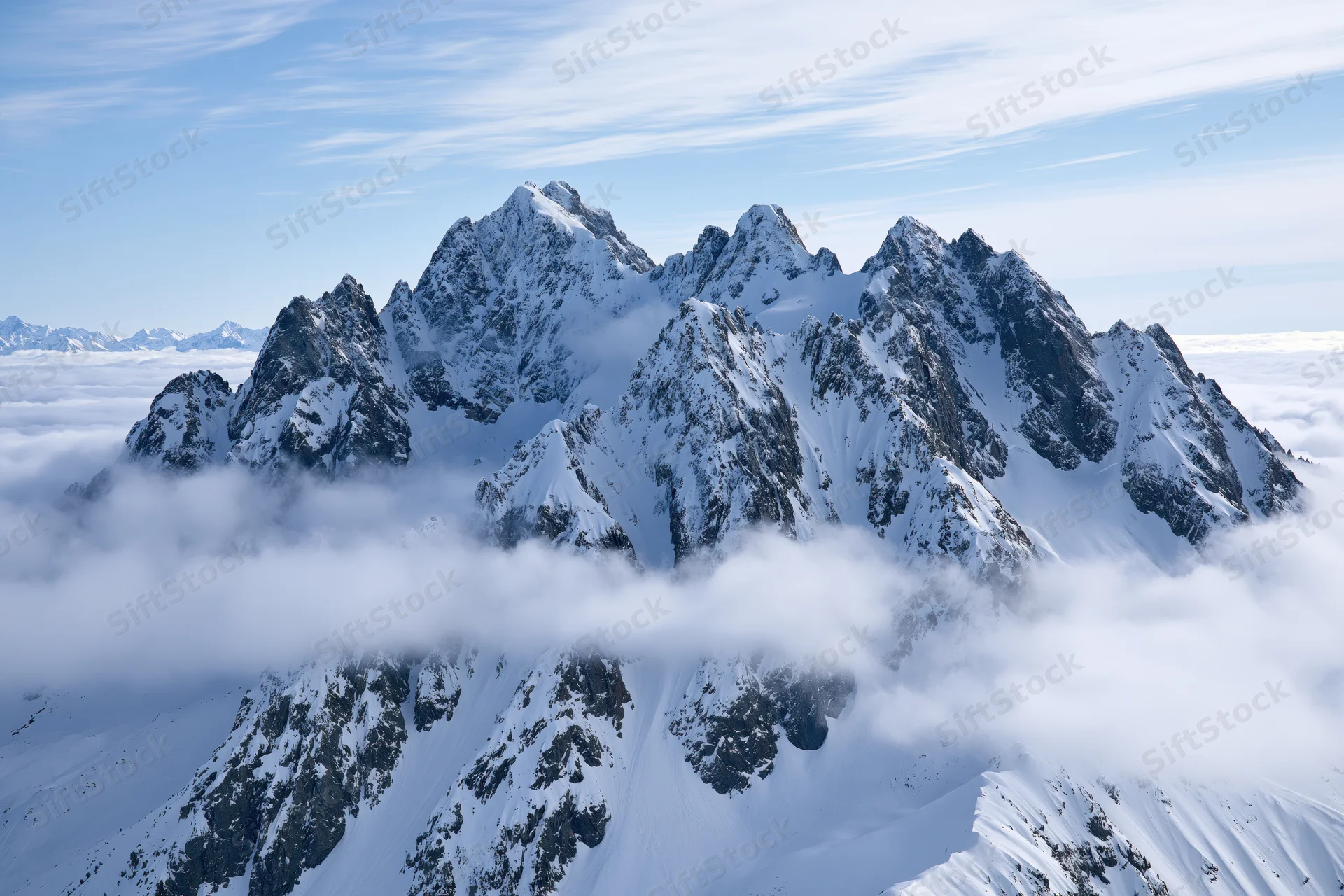 Snow-covered alpine peaks rising above a sea of low clouds under a clear blue sky