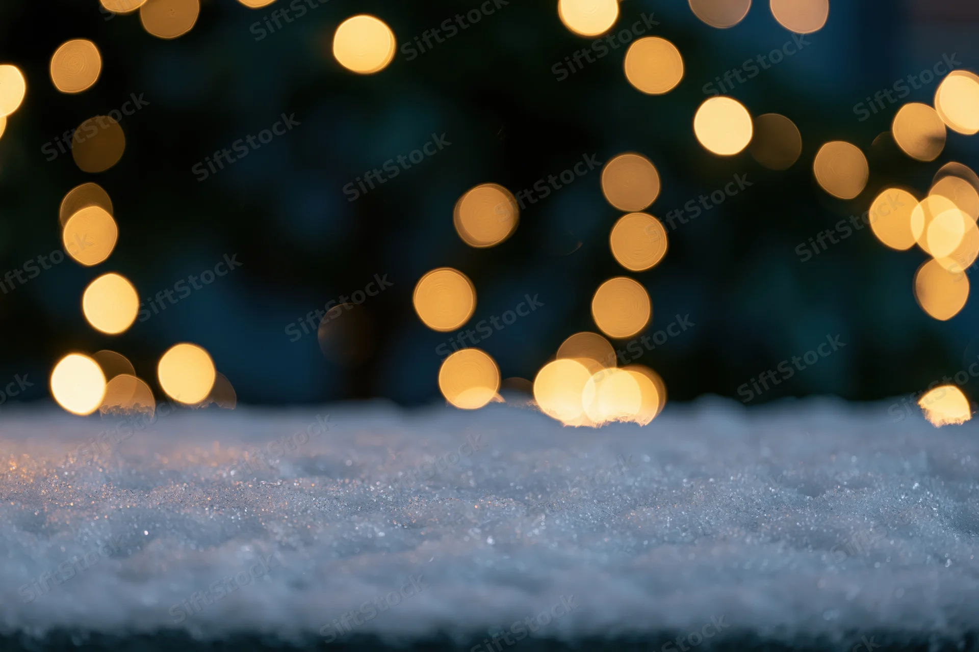 Snow-covered ground with blurred golden lights in the background at night