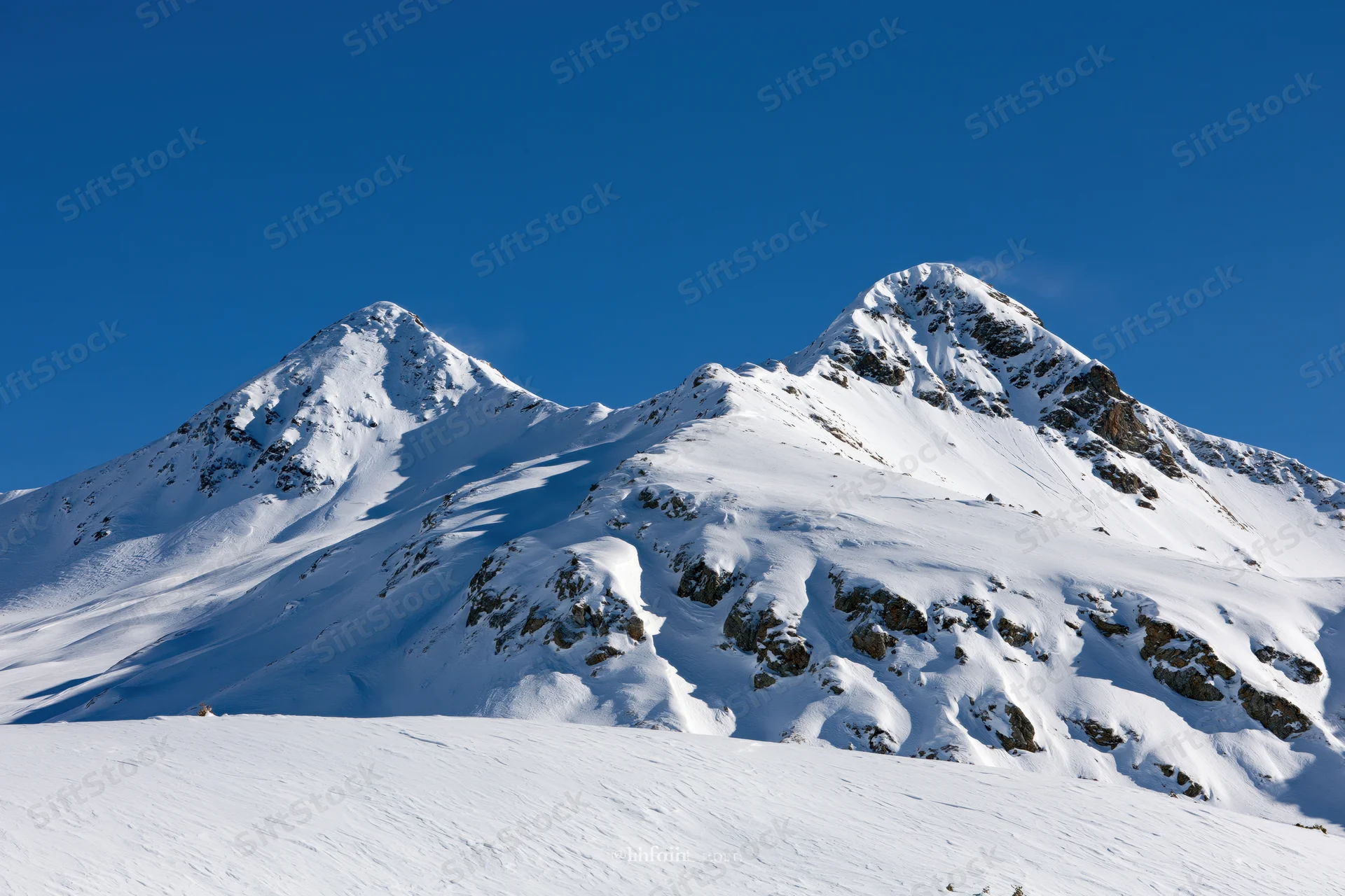 Snow-covered twin mountain peaks rising against a clear deep blue sky in alpine winter landscape
