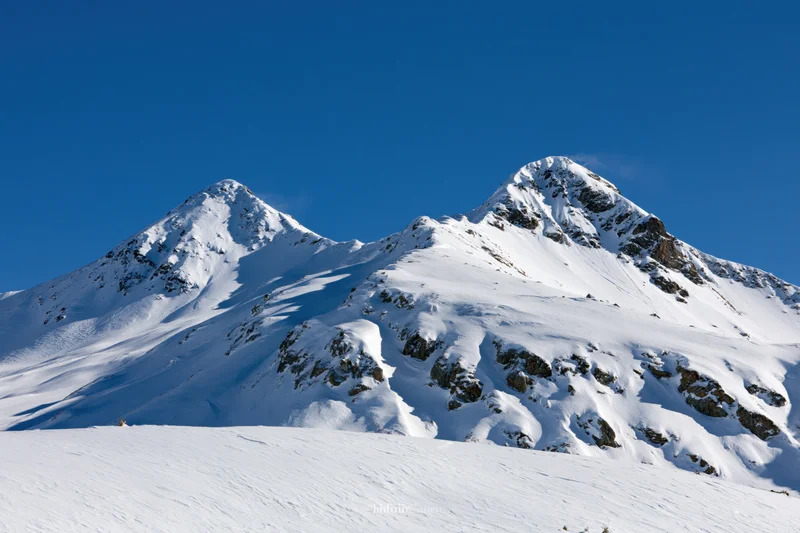Snow-covered twin mountain peaks rising against a clear deep blue sky in alpine winter landscape