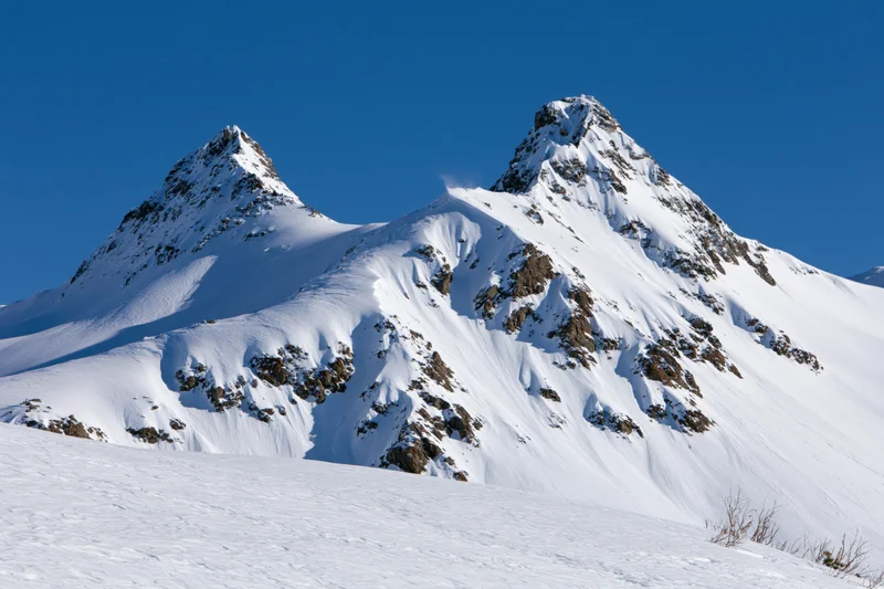 Snow-covered twin mountain peaks rising against a clear blue sky