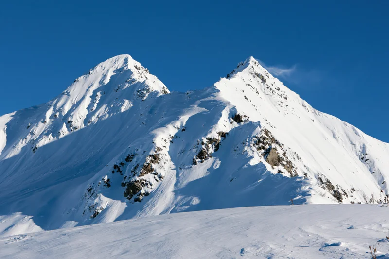 Snow-covered twin mountain peaks rising against a clear blue sky in alpine winter landscape