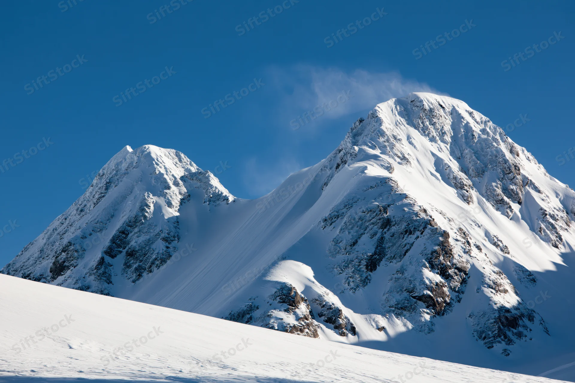 Snow-covered twin mountain peaks rising against a clear blue sky in a winter alpine landscape