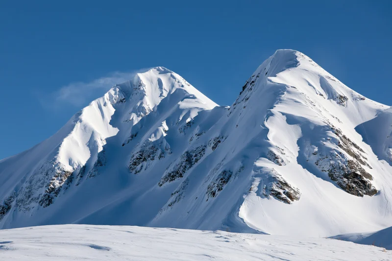 Snow-covered twin mountain peaks rising against a clear deep blue sky in alpine winter landscape