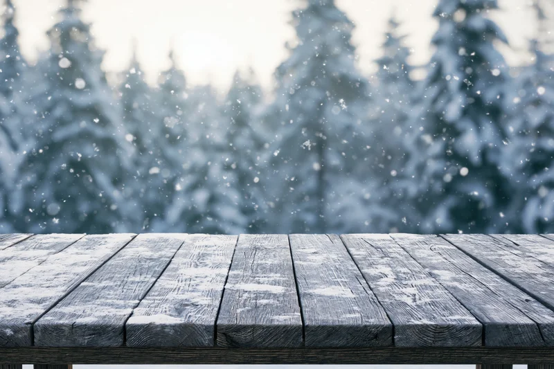 Snow-dusted wooden table in front of a snowy forest during winter