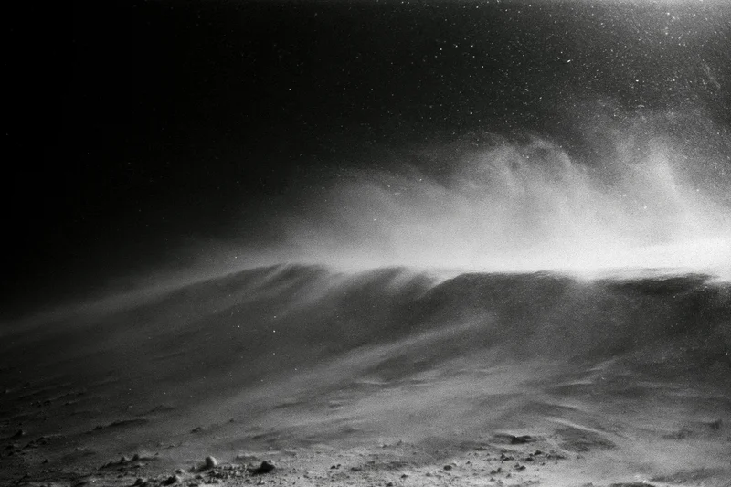 Snow blowing across a high alpine ridge at night under a starry sky