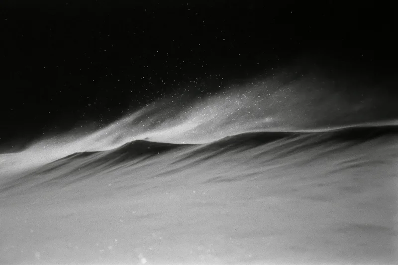 Snow blowing across a high alpine ridge at night under a starry sky