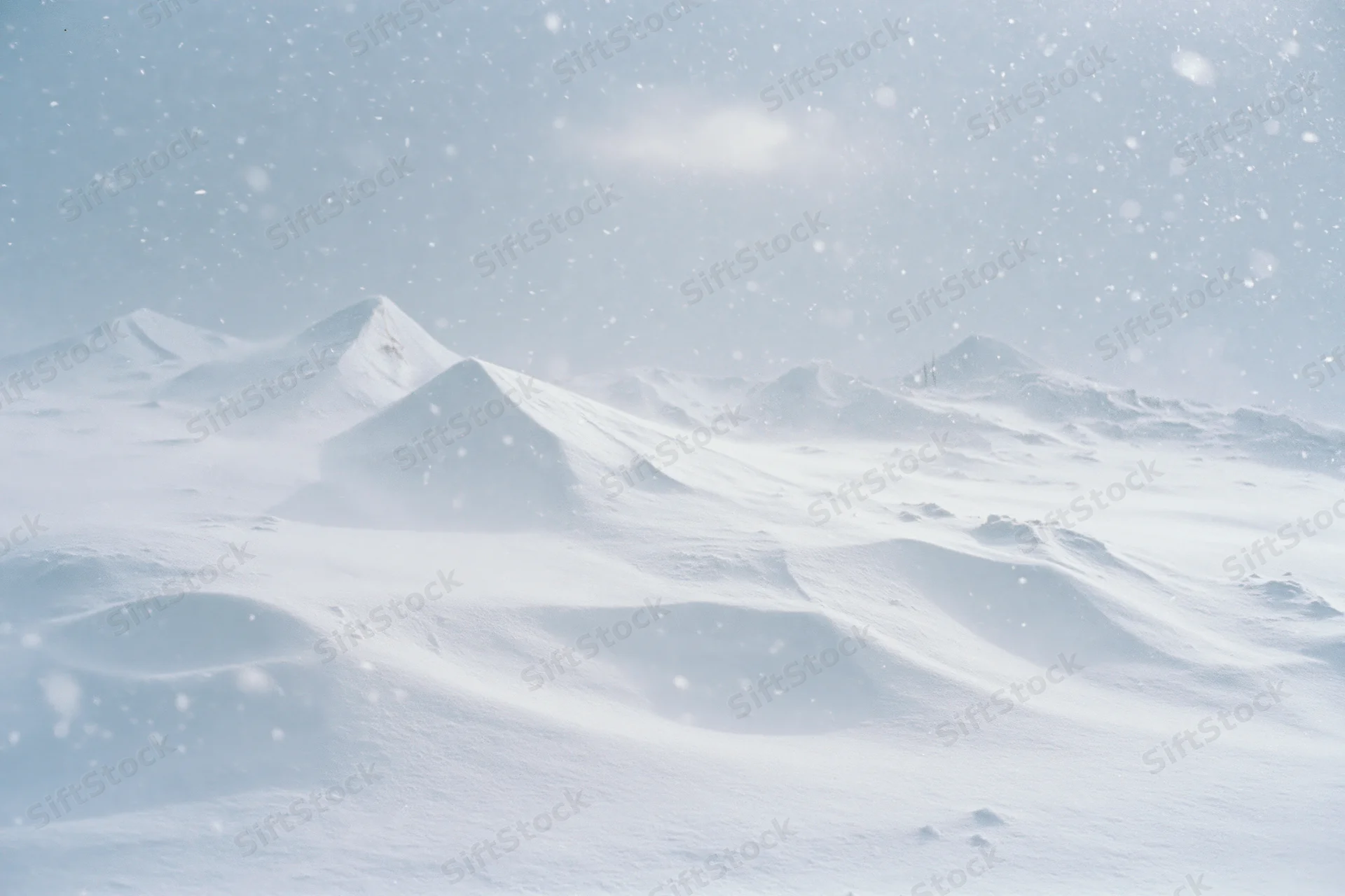 Snow-covered mountains under falling snow with drifts and mounds in foreground