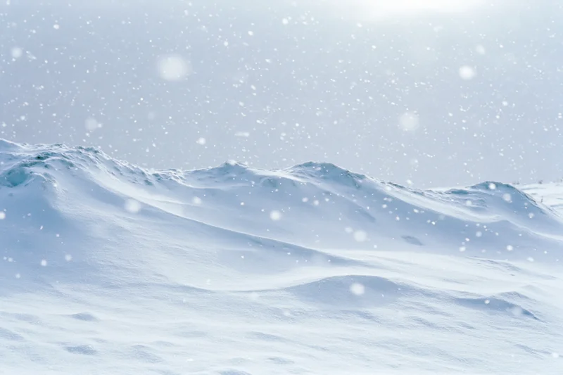 Snow drifts and mounds filling the lower third of the frame under falling snow with overcast sky