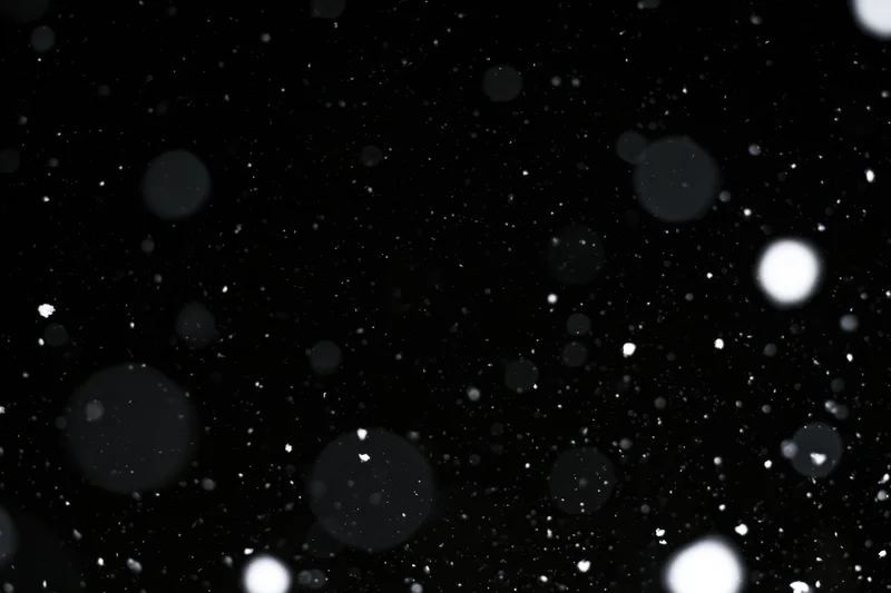 Snow falling against a black night sky in close-up abstract view