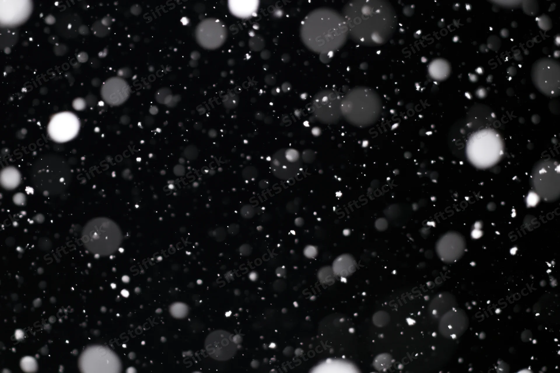 Snow falling against a black night sky in close-up abstract view