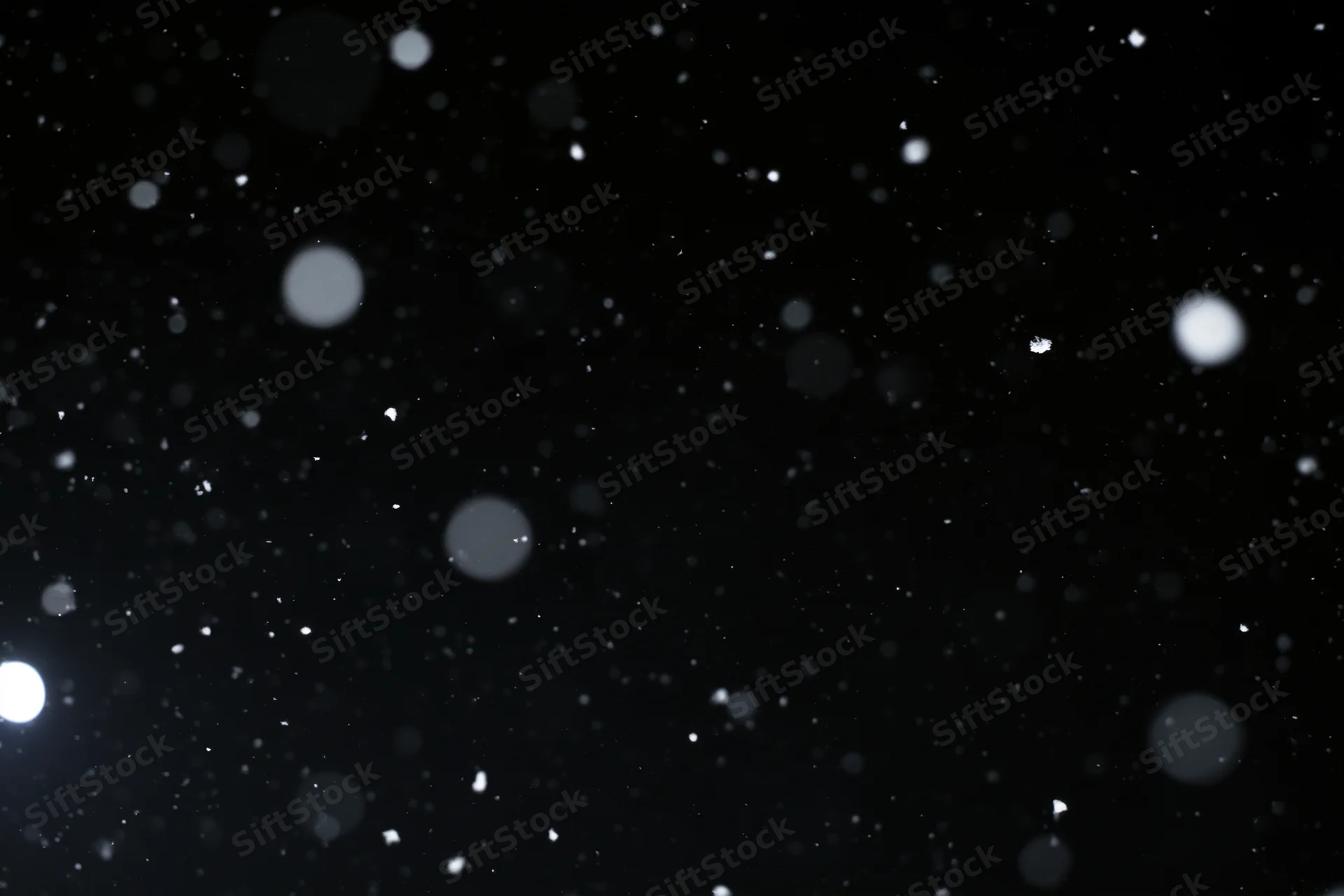 Snow falling against a black night sky with bokeh highlights