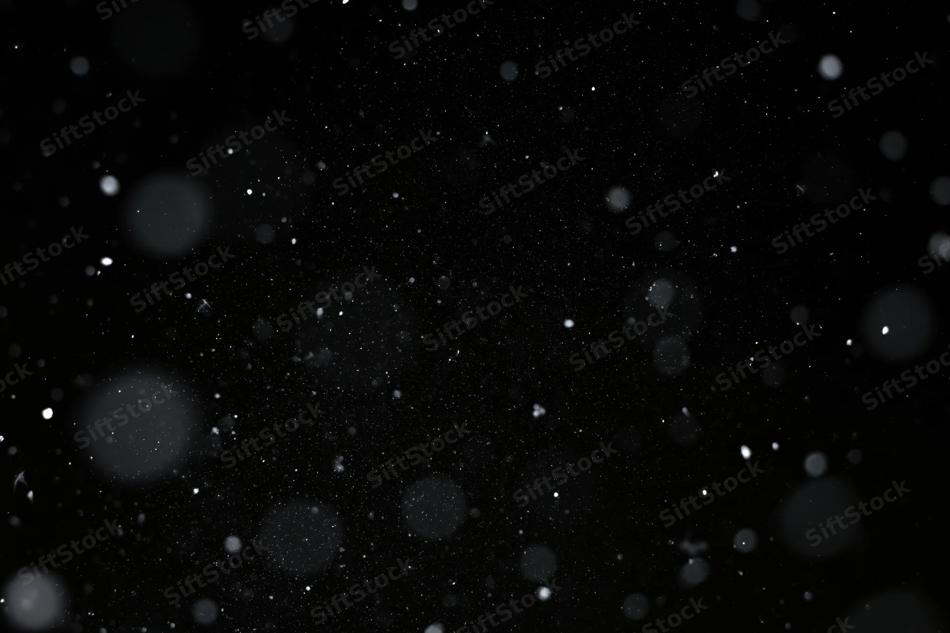 Snow and dust particles falling against a pure black background