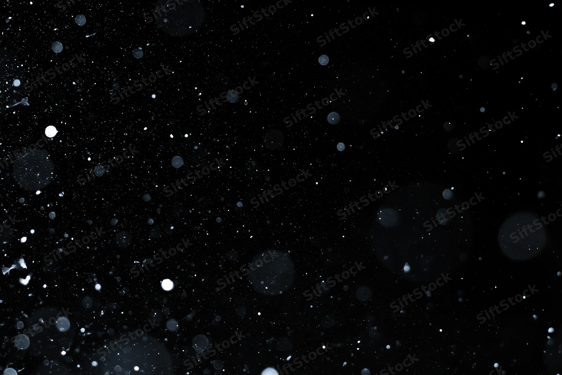 Snow and dust particles falling against a pure black background