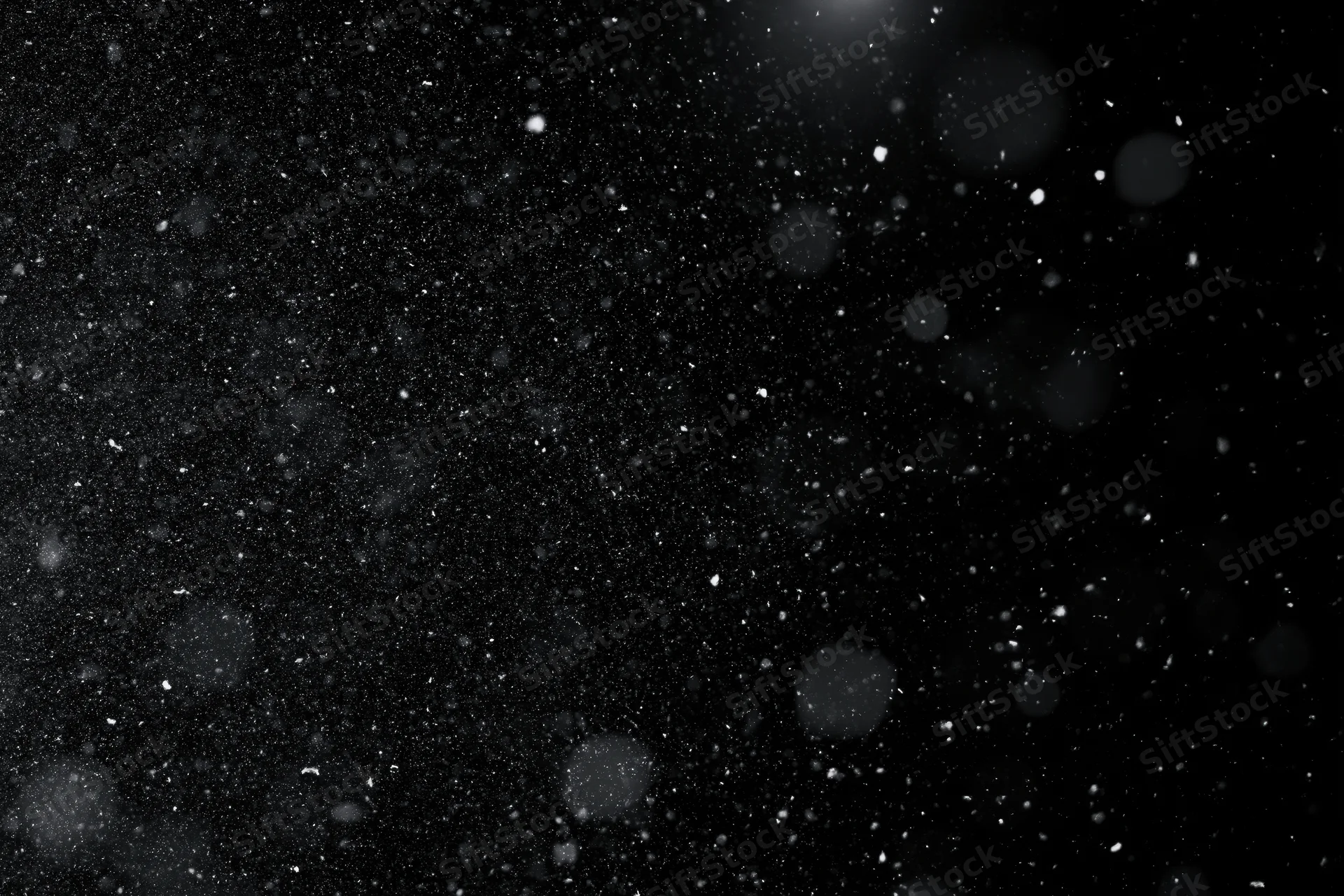 Snow and dust particles floating in mid-air against a black background
