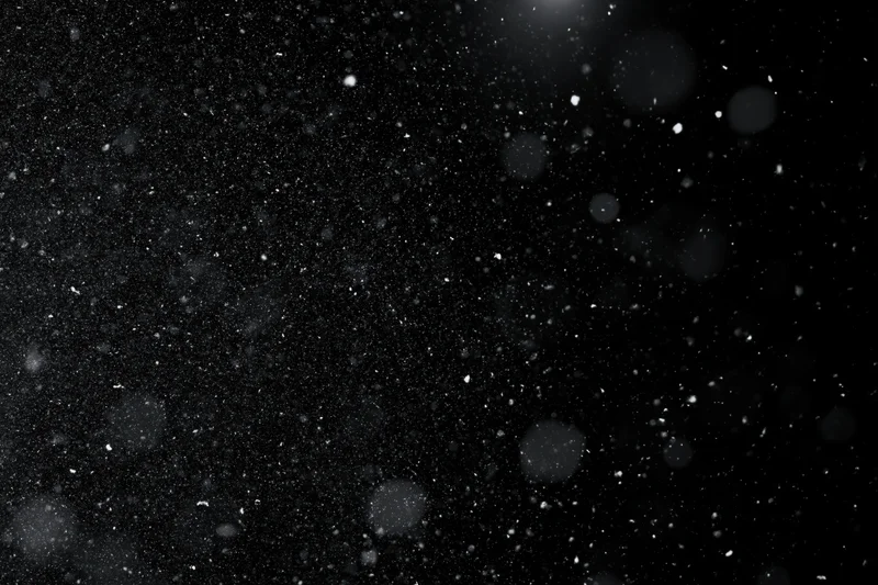 Snow and dust particles floating in mid-air against a black background