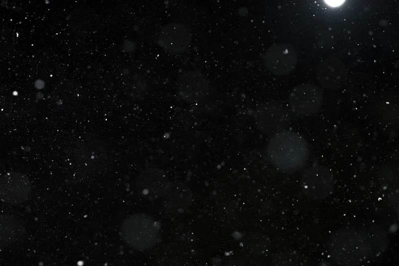 Snow particles floating in dark space against black background
