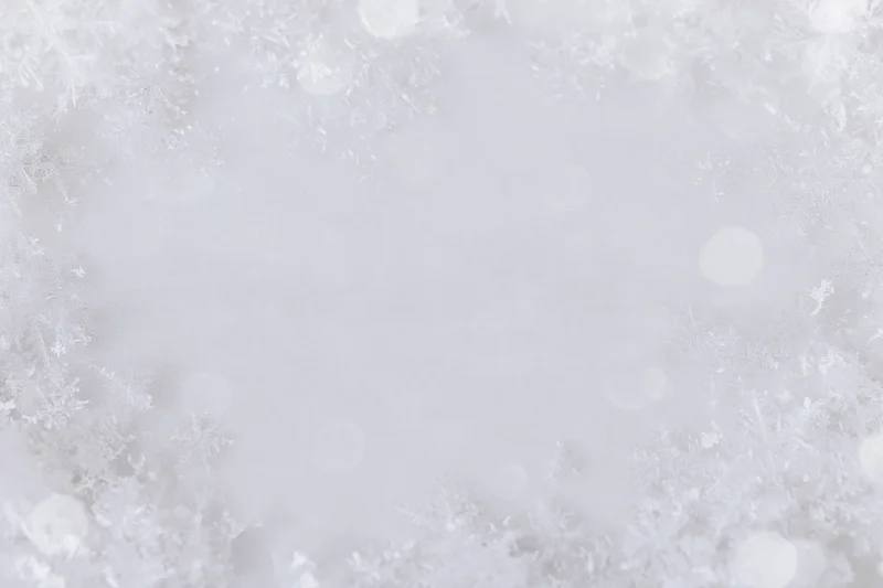 Snowflakes and bokeh scattered across a white frame with copyspace in center