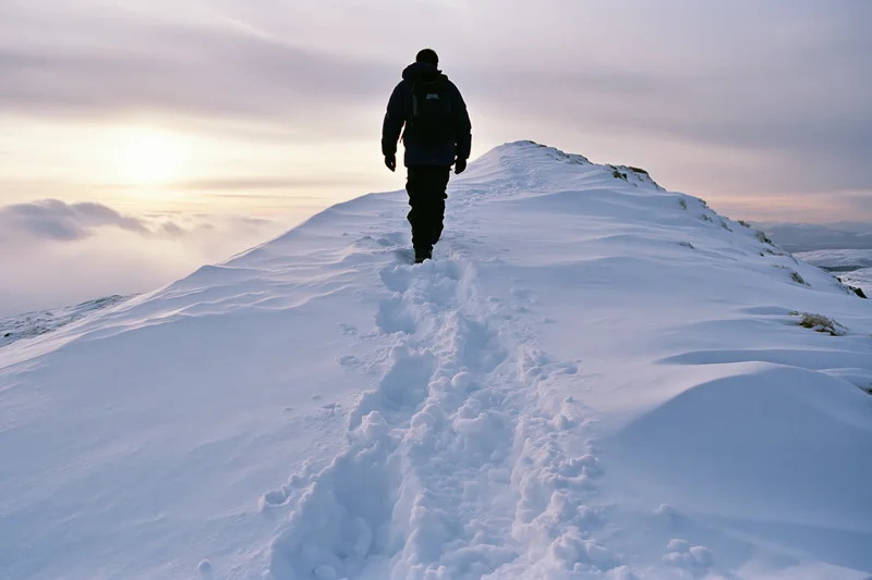 Hiker walking along snow-covered mountain ridge leaving footprints in the snow